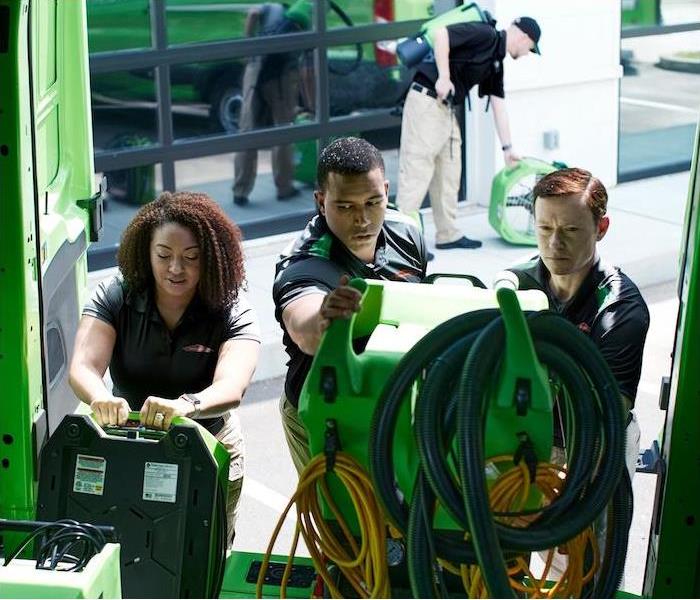 Three SERVPRO employees unloading equipment out of a green van.