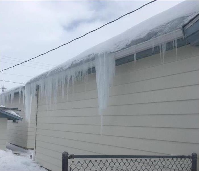 Outside from a house, the roof is covered with snow and there is an ice dam in the edge of the roof